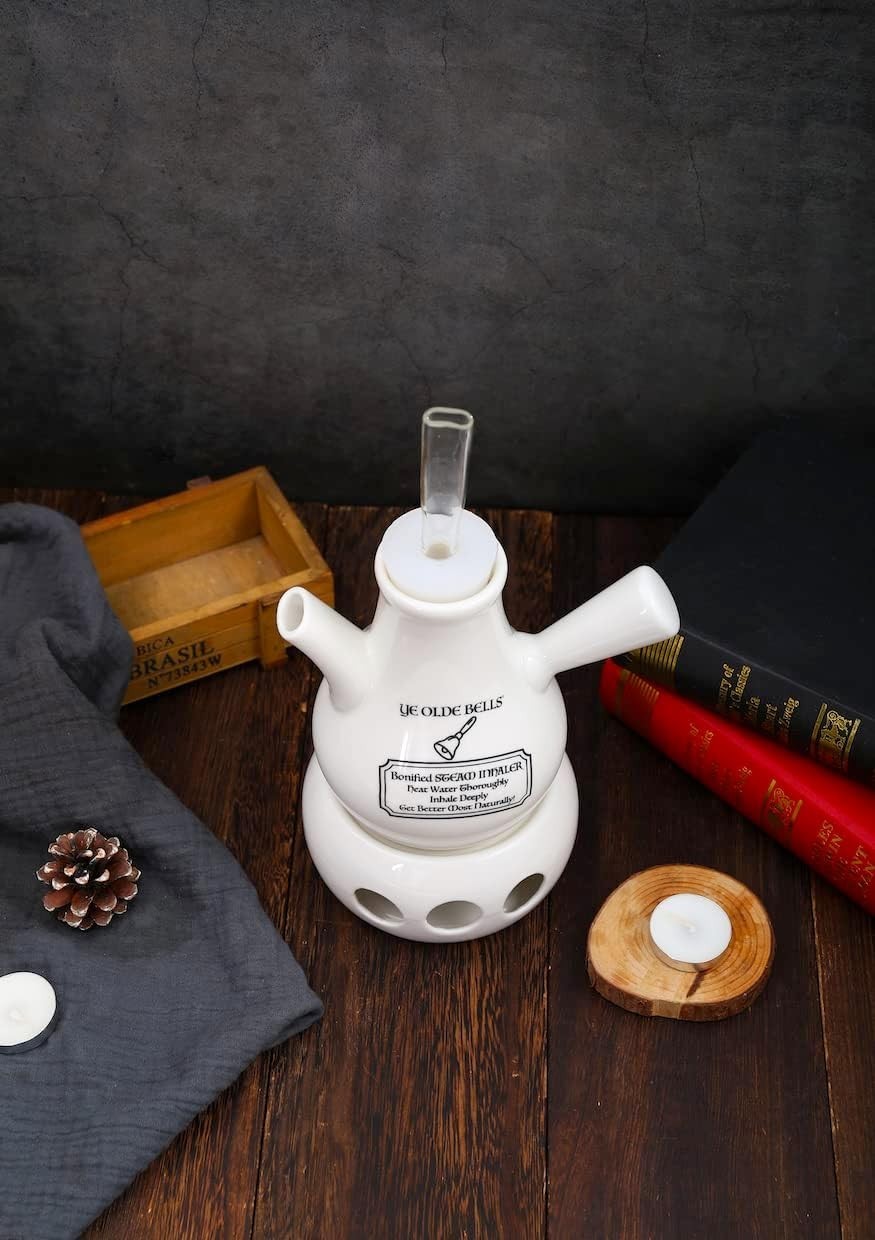 Victorian-style ceramic steam inhaler by Ye Olde Bells beside vintage books and a lit tealight